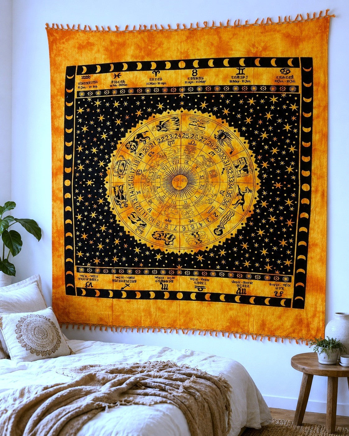 A large yellow and black celestial tapestry with an astrological zodiac wheel, moon phases, and stars, hanging on a white wall above a bed in a bedroom setting.