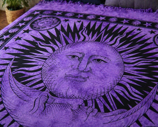 A purple and black tapestry featuring a detailed celestial design with a sun face, crescent moon, stars, and sun phases, shown draped over furniture in a home setting.